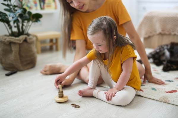 Child with needs playing on the floor with woman